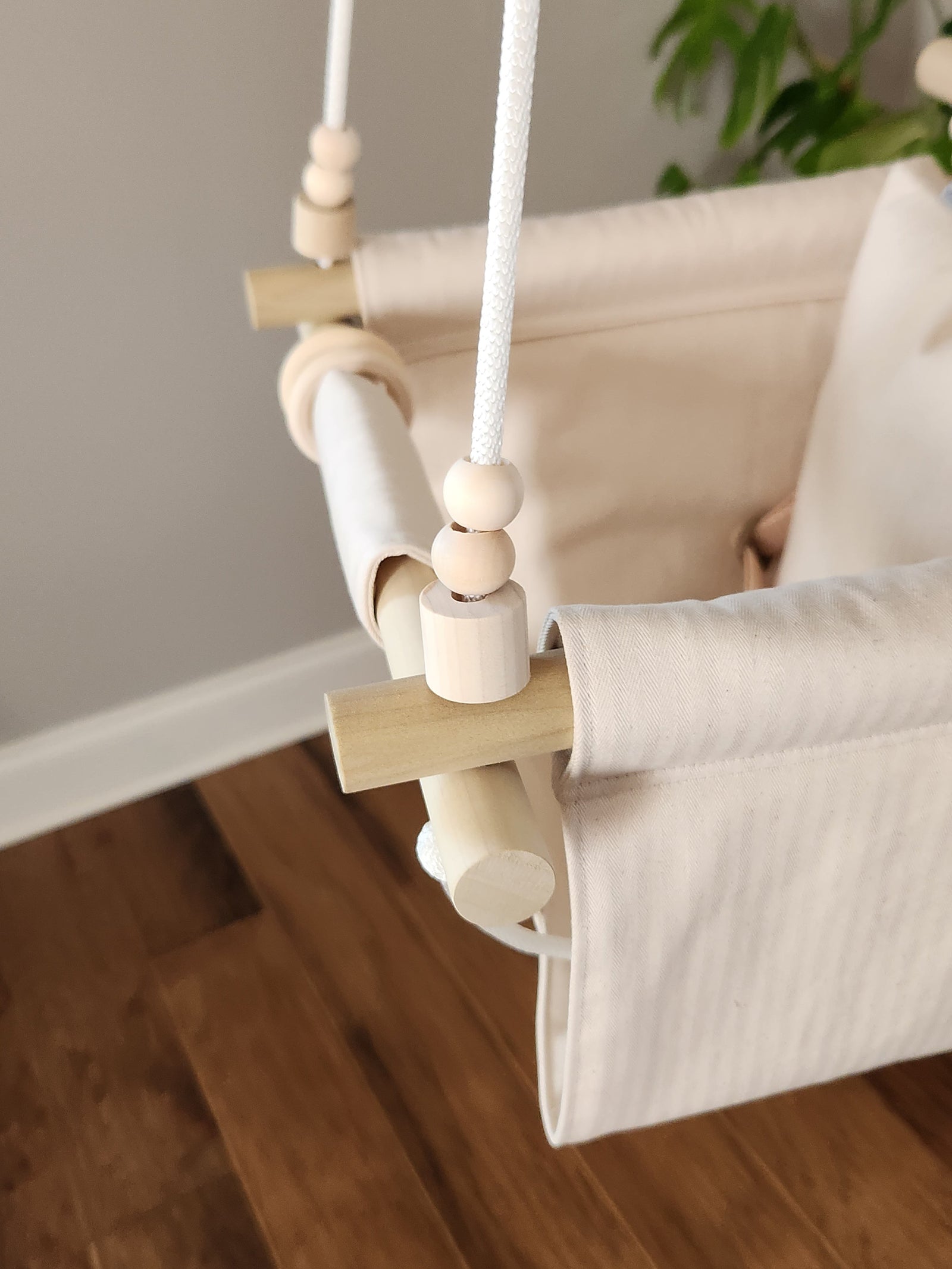 Children's swing hanging against a plain wall with plants on either side.