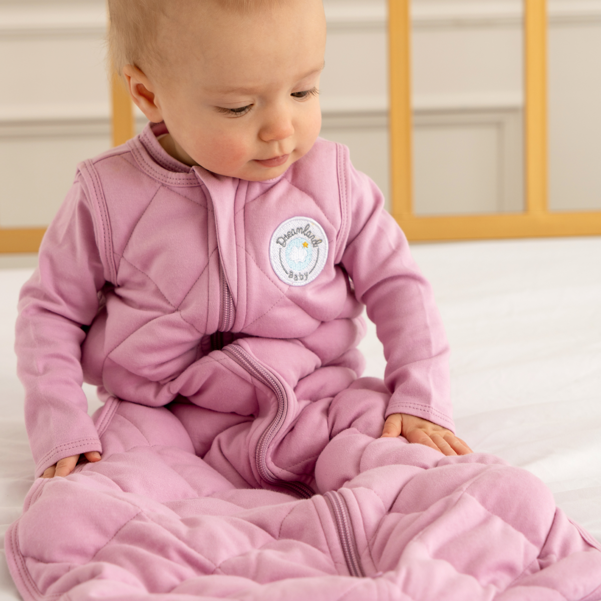 Pink quilted baby sleeping sack swaddle with a brand logo on a white background