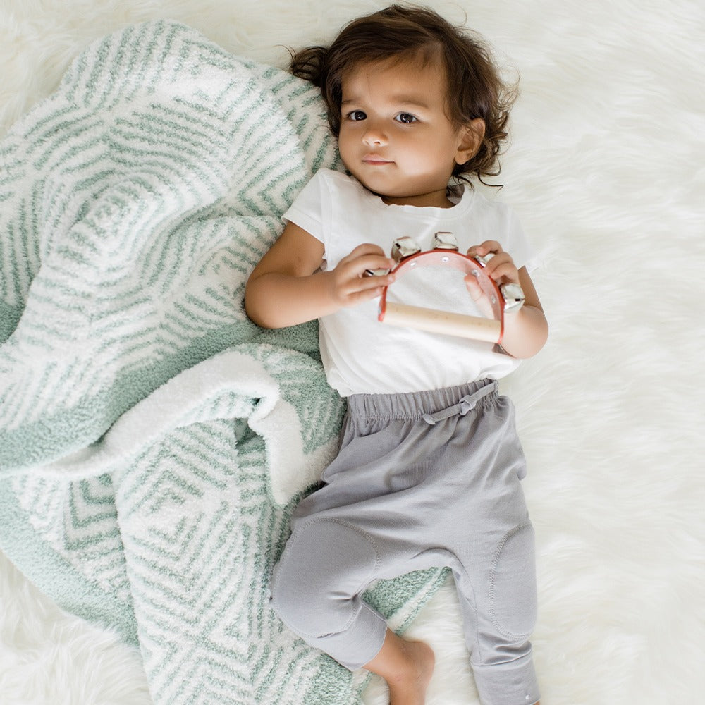 A sage green blanket on a gray and white geometric animal patterned blanket.