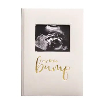 A person holding a white pregnancy journal with 'My Little Bump' printed in gold foil on the cover, featuring a photo insert of a sonogram.