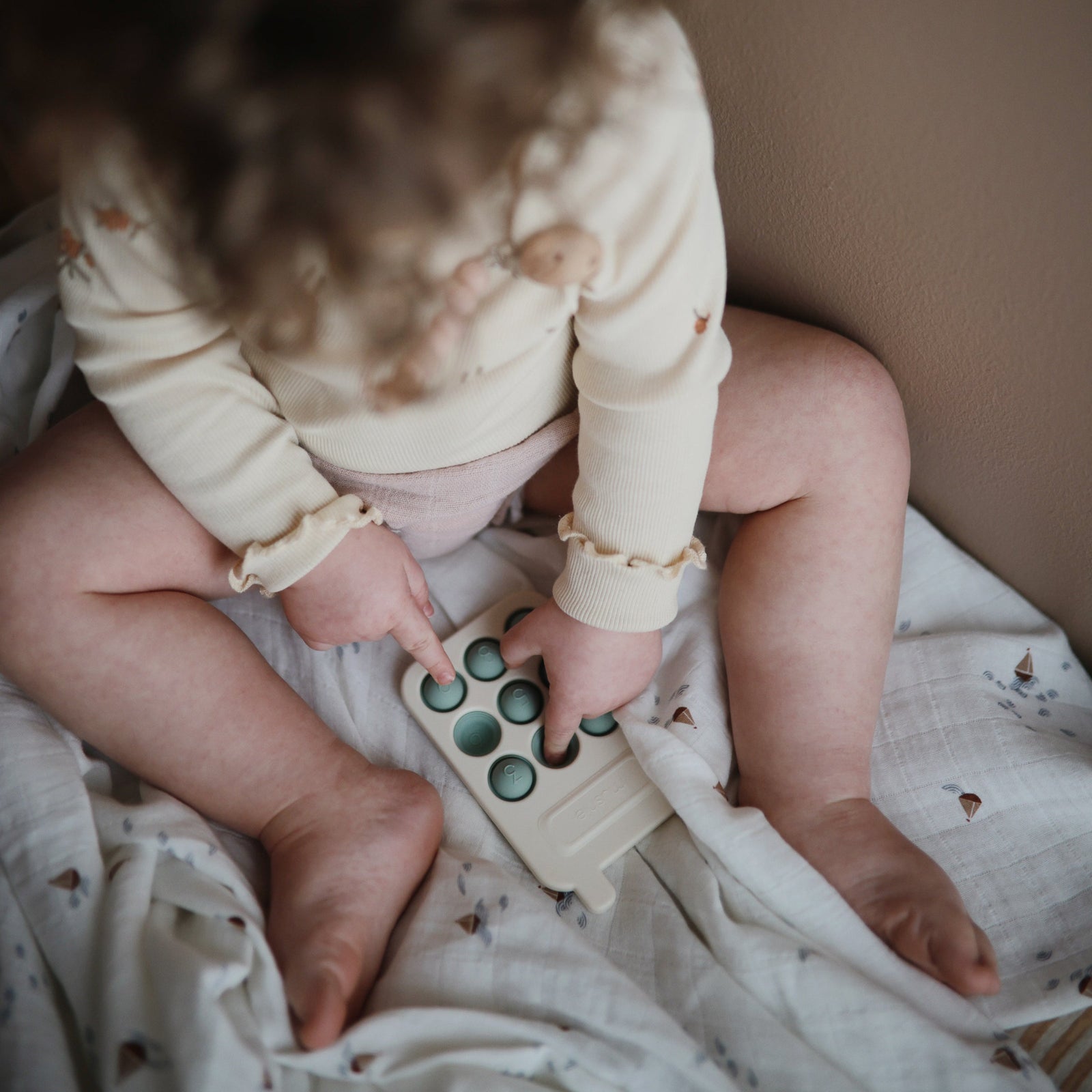 A soft silicone phone-shaped toy with numbered buttons in various shades of green and a BPA-free plastic frame.